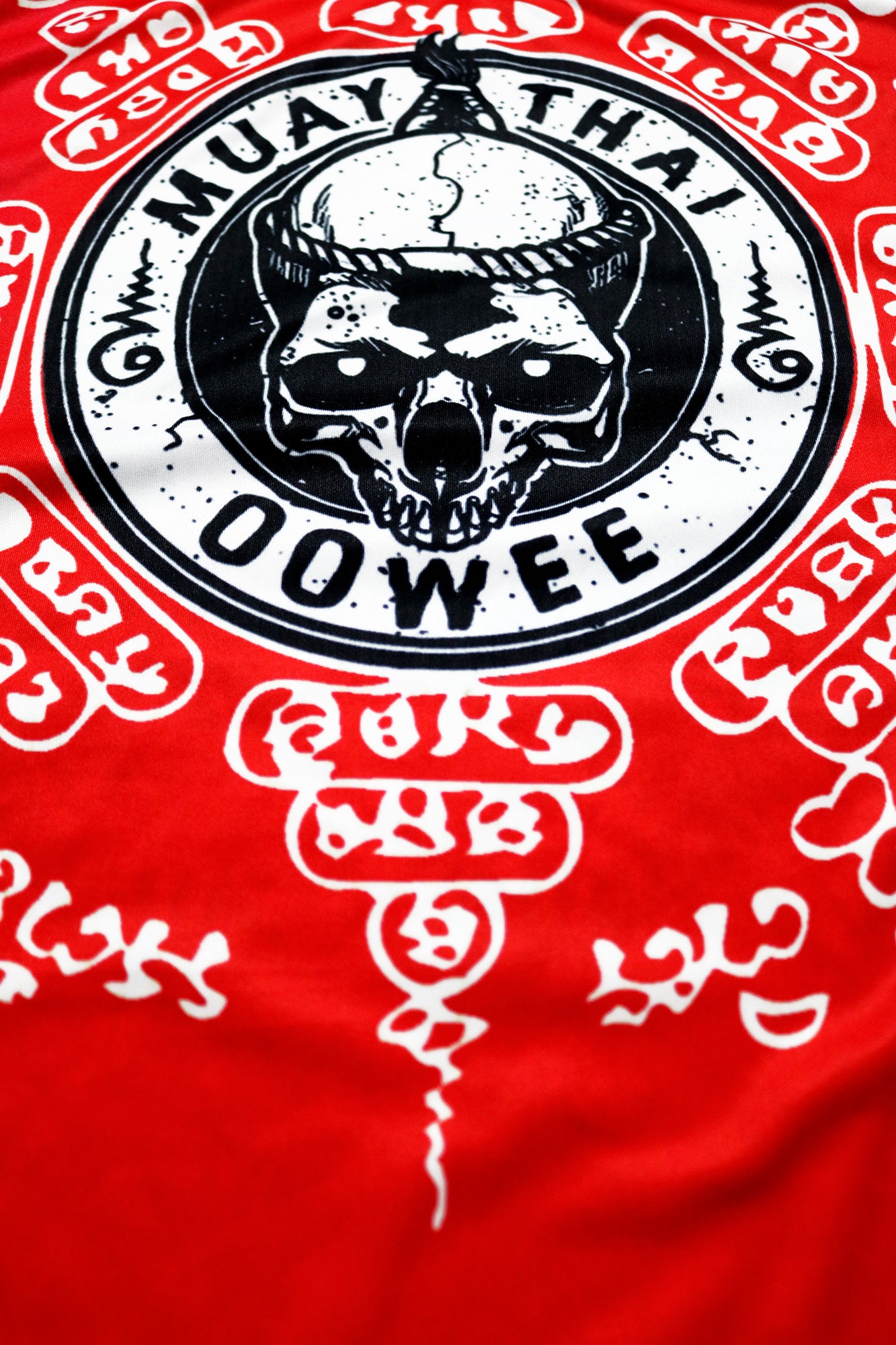 Close-up of the front graphic on a red Muay Thai tank top featuring a black and white skull, surrounded by traditional Sak Yant symbols and Thai script, emphasizing the intricate design details.