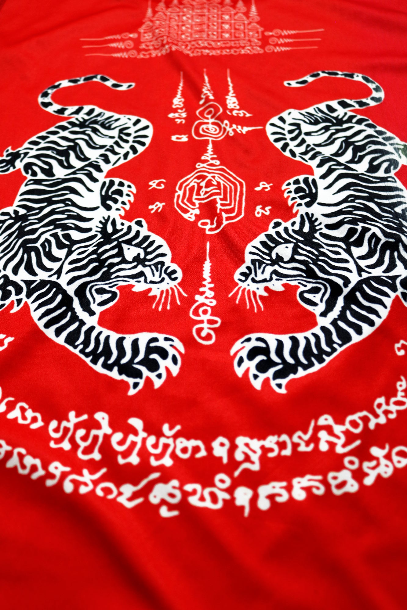 Close-up of the backside graphic on a red Muay Thai tank top featuring two black and white tigers, surrounded by traditional Sak Yant symbols and Thai script, highlighting the detailed design for protection and strength.