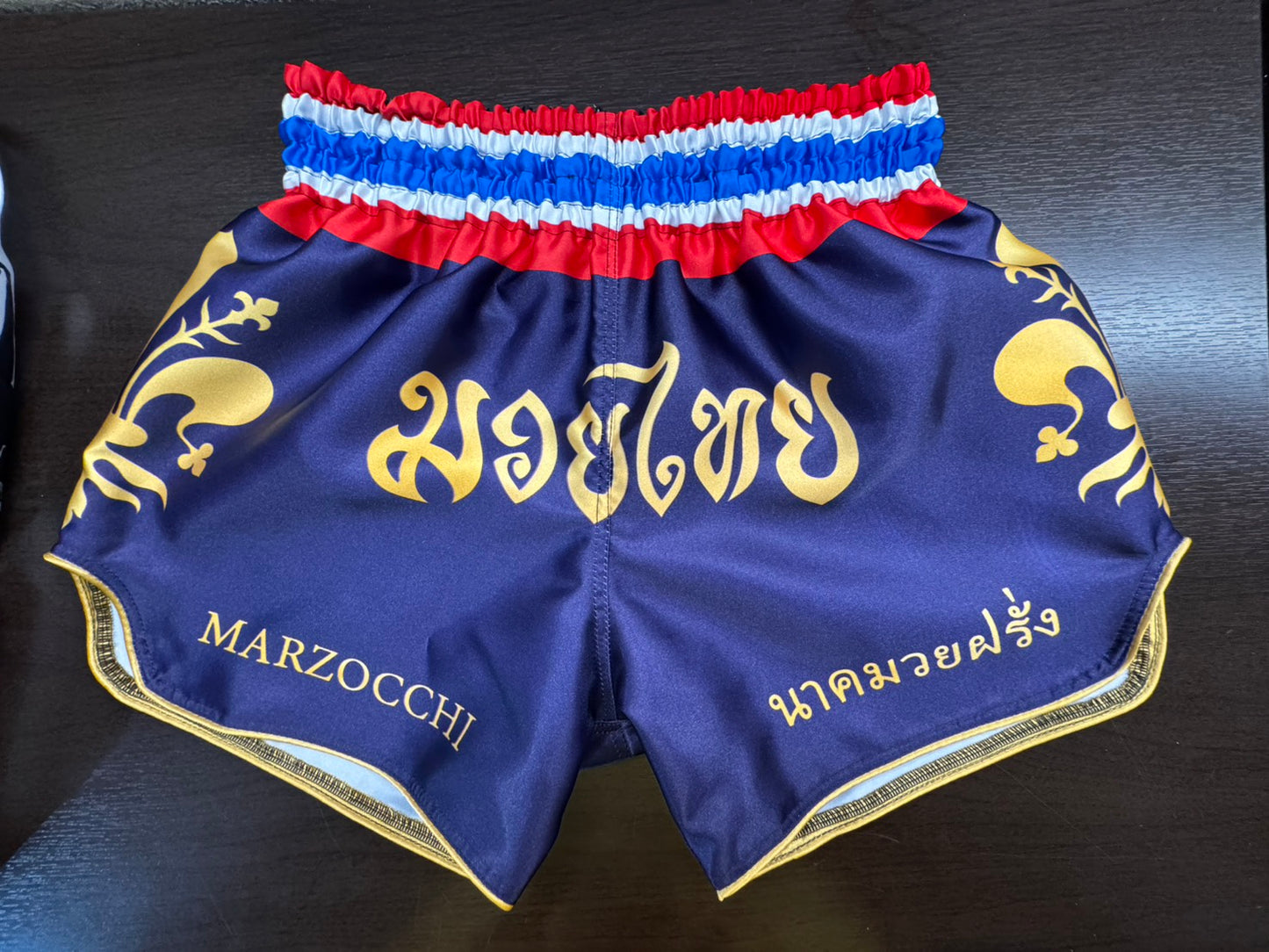 custom made muay thai shorts with blue / purble body and golden font and logos. thai flag waist